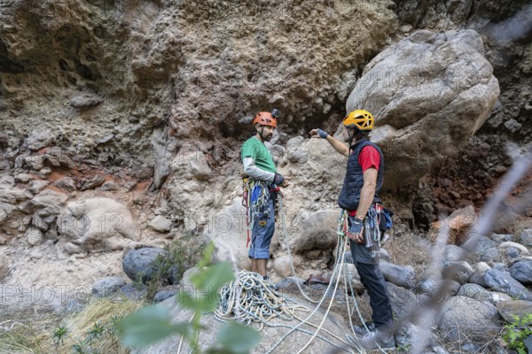 Two climbers prepare for a traditional climbing adventure in a rugged natural landscape, surrounded by rock formations. They discuss routes, gear, and safety measures