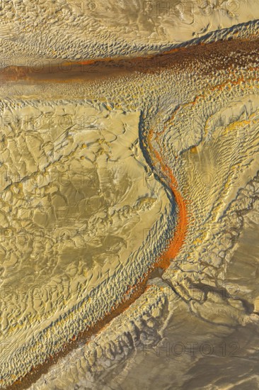 Aerial shot showing a textured, sandy desert terrain with orange streaks creating a river like pattern across the surface, capturing natural abstract art