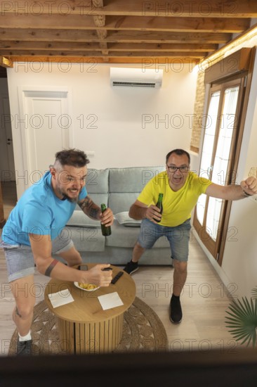 Friends reacting with excitement after a goal while watching a live sports match at home. Spontaneous celebration, energy and friendship