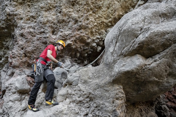 A climber scales a rugged rock face using traditional techniques, surrounded by impressive natural scenery. Equipped with safety gear, he navigates the challenging terrain skillfully