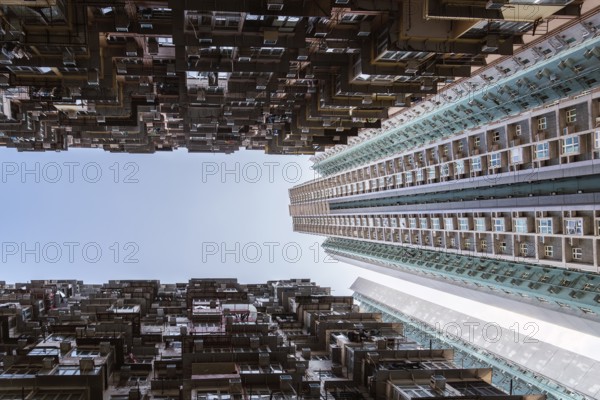 Low angle of a striking vertical view of dense residential towers in Hong Kong, showcasing the city's unique urban architecture and overpopulation, framed by a clear blue sky above