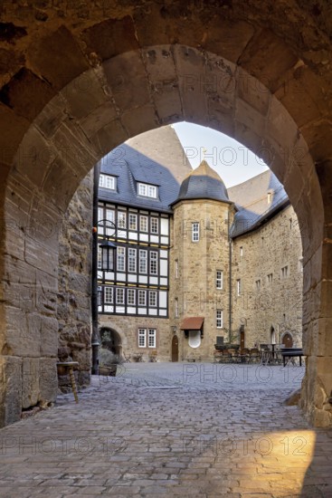 Through a stone Tor tor you can see a courtyard with a half-timbered house in the warm light of the evening, The courtyard of Spangenberg Castle