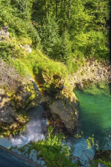 Stunning rainbow forming over waterfall cascading into turquoise water in vintgar gorge near bled, slovenia, a popular tourist destination