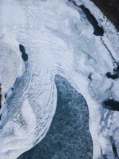 Aerial view of a frozen Icelandic landscape and rivers showcasing intricate icy patterns and textures. The serene winter scene highlights the remote beauty and wild nature of Iceland
