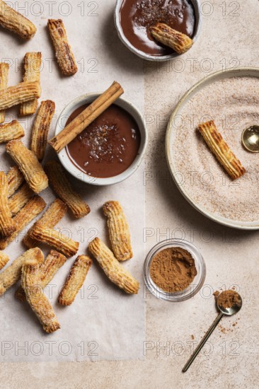 Top view of homemade churros generously dusted with sugar and cinnamon, accompanied by a rich chocolate dipping sauce and a sprinkle of sea salt, all presented on a textured ceramic background for a moody feel
