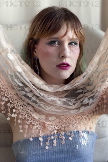 A woman with vibrant makeup and a sequined top poses gracefully, holding a delicate lace shawl Her expression conveys confidence and style, blending modernity and elegance