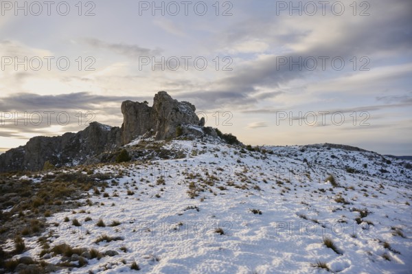 Stunning panoramic view of Montcabrer, Spain, showcasing a snow-covered mountain landscape at dusk, with rocky outcrops and a serene sky filled with clouds