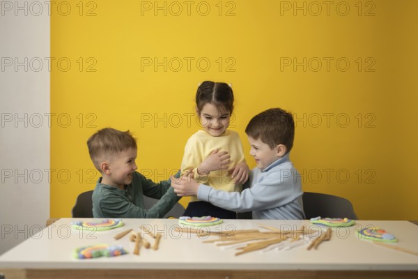 Three children engage in a playful educational lesson in a vibrant yellow classroom. Smiling faces and colorful clay crafts create an atmosphere of joyful learning and imagination