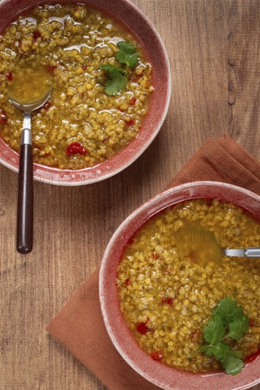 Enjoy a hearty grain soup featuring a vibrant mix of ingredients served in two rustic bowls, garnished with fresh herbs, resting on a warm wooden surface