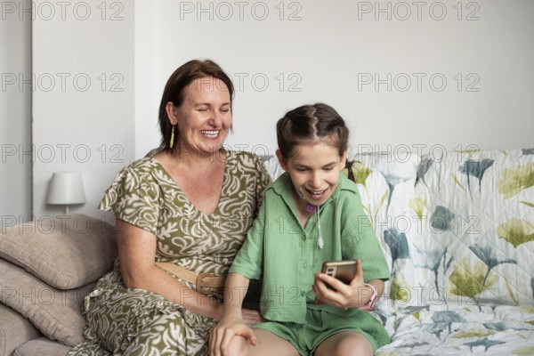 A joyful scene of a mother and her disabled daughter, who has a tracheostomy, sitting inside and sharing moments of happiness while looking at a smartphone
