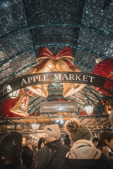 Visitors to Apple Market surrounded by Christmas bells and a sign with handmade art & design, AppleMarket, London, Great Britain