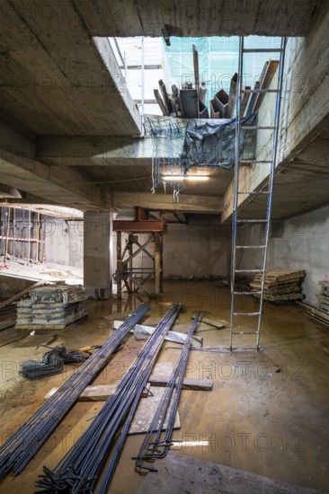A construction site with steel beams, wooden planks, and a blue ladder. The area is lit naturally, with tools scattered, reflecting a work-in-progress scenario