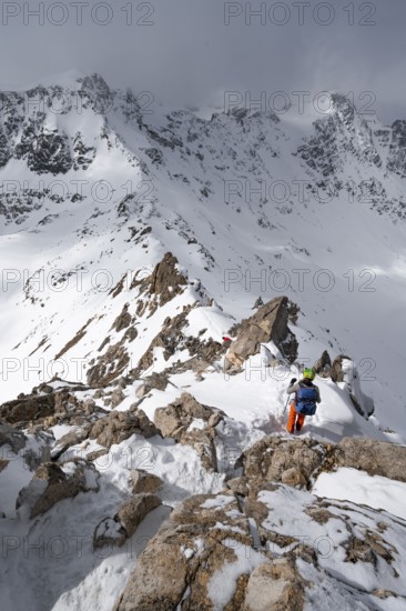 Mountaineer descending the narrow ridge of Piz Laviner, view of mountain panorama in wintry mountain landscape with dramatic clouds, Grisons Haute Route, Albula Alps, Rhaetian Alps, Grisons, Eastern Switzerland, Switzerland
