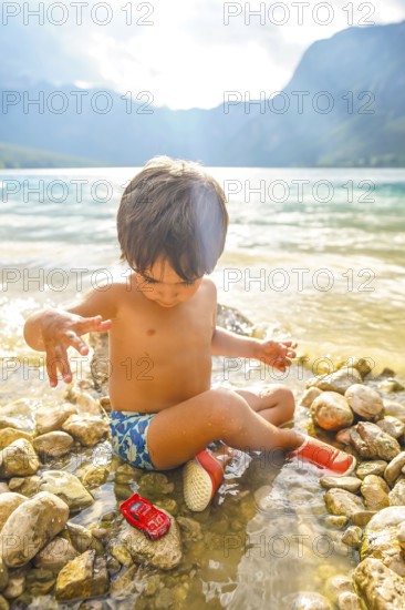 Young child enjoying summer vacation, playing with a toy car by the water's edge of lake bohinj in slovenia