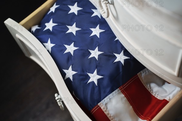 A folded American flag rests neatly inside a white wooden drawer, symbolizing national pride and heritage. The stars and stripes evoke feelings of patriotism and respect
