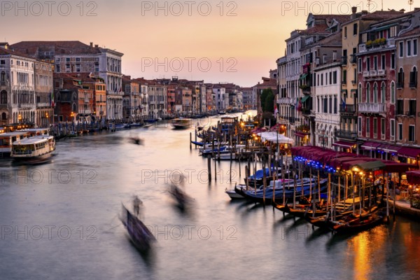 View of the Grand Canal with gondoliers at sunset, picturesque evening mood with illuminated palazzos on the canal, long exposure, view from the Rialto Bridge, Venice, Veneto, Italy