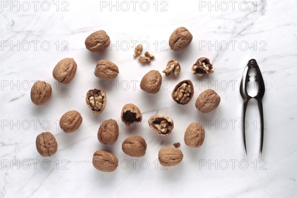 Whole and cracked walnuts scattered on a marble surface, next to a shiny metal nutcracker. The composition offers a rustic and culinary aesthetic