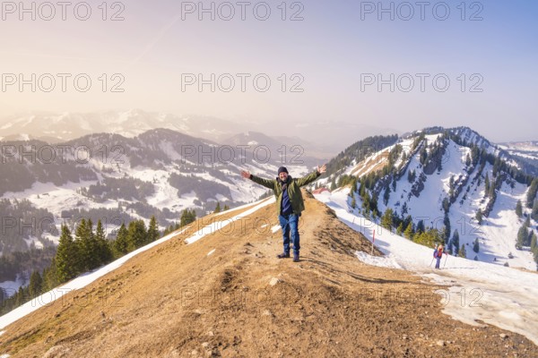 A hiker with outstretched arms enjoys the view from the mountain summit with deep snow and clear skies, Hochgrat Mountains, Allgäu Alps, Oberreute, Germany