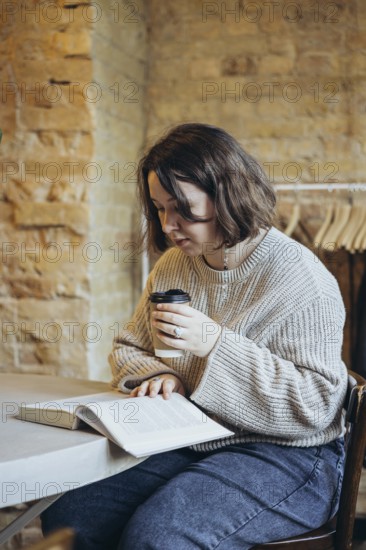 A young woman sits in a charming bookstore, engrossed in a book, while enjoying a hot coffee The warm ambiance and rustic brick walls add to the cozy atmosphere