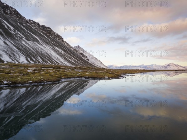 Breathtaking winter landscape of Iceland featuring snow-capped mountains and their reflection in serene water under a softly colored sky, capturing nature's tranquility