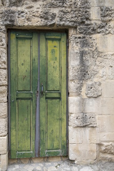 Old green wooden door in a weathered stone wall. Rustic and historic appearance, Matera historic centre, Basilicata, southern Italy, Italy