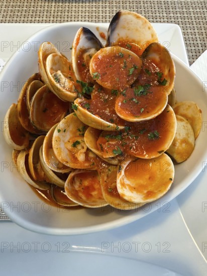 Fresh clams cooked in a spicy tomato sauce, garnished with chopped parsley, served in a Thai cafe