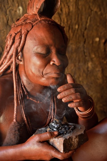 Traditionally dressed Himba woman in her hut, applying perfume, Purros Traditional Village, Purros, Kaokoland, Kunene, Namibia