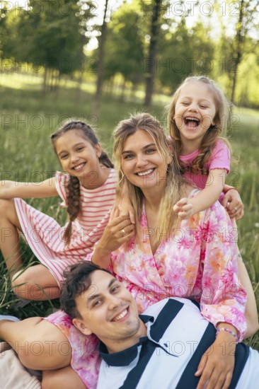 A joyful family shares a happy moment together in a lush green park, laughing and embracing. The carefree atmosphere highlights love, connection, and the beauty of family life