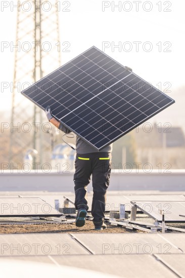 Person carrying solar module on a sunny roof next to a power pole, ready for installation, PV installation at OBI Baumarkt, Mühlacker, Enzkreis, Germany