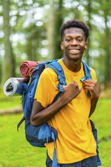 Vertical portrait of a young african man having a walk with a backpack through beautiful nature