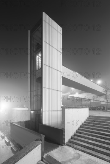 A modern, isolated urban elevator shrouded in thick fog at night captures a both mysterious and architectural essence in a city setting