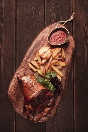 Pork knuckle, in soy-honey sauce, with fried potatoes, on a wooden chopping board, homemade, no people
