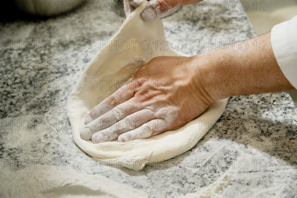 Cropped unrecognizable person kneading fresh pizza dough on a flour-dusted marble countertop, focusing on handwork and ingredients in the kitchen