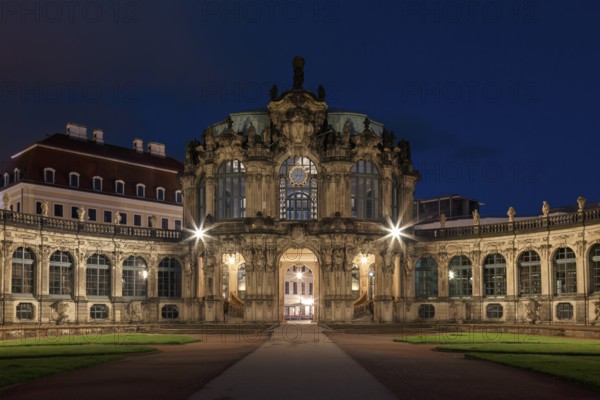 The Zwinger Palace in Dresden, Germany, is beautifully illuminated under a deep blue night sky. This baroque architecture marvel features symmetrical pathways and ornate facades