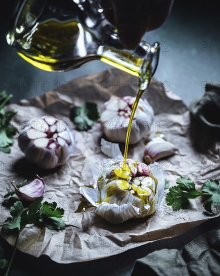 Close-up of garlic bulbs drizzled with olive oil, surrounded by fresh herbs on crumpled parchment paper. The scene captures a rustic, gourmet atmosphere perfect for cooking themes