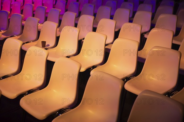 Rows of empty seats at a conference of AI in Amsterdam by vibrant purple and orange lights. The smooth curves and colors create a dynamic, inviting atmosphere