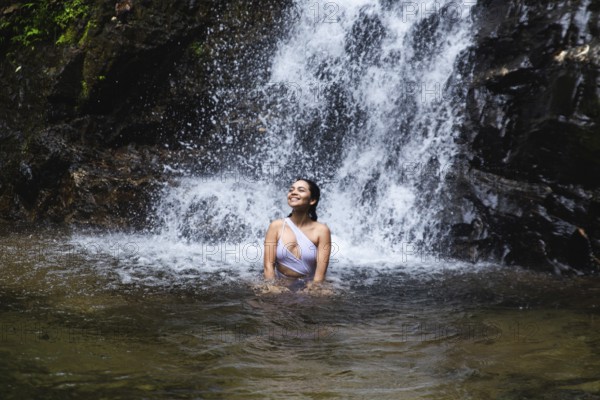 Young Ecuadorian woman enjoys blissfully in a natural pool under a waterfall in the Choco Andino rainforest in Ecuador. The image captures her connection with the lush, tropical landscape