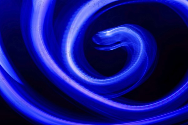 A mesmerizing abstract composition featuring swirling blue neon lights against a deep black background. The vibrant light trails create a dynamic, fluid effect