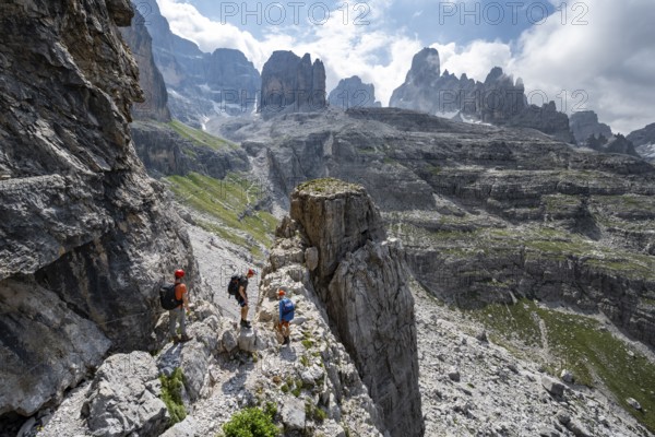 Three mountaineers in front of picturesque mountain landscape with rocky peaks, Via Ferrata SOSAT via ferrata, Cima Tosa summit in the back, Brenta Mountains, Trentino, Italy