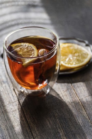 A warm glass of English tea, infused with a slice of lemon, presented on a rustic wooden table, capturing the essence of a cozy afternoon