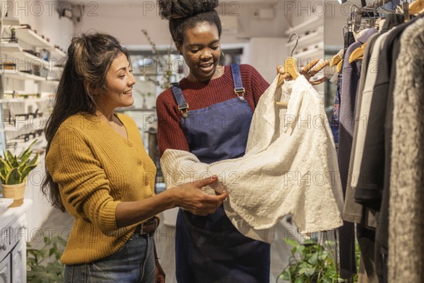 A boutique employee assists a customer in choosing clothing. They are smiling and engaged while discussing a white garment, showcasing a friendly shopping atmosphere