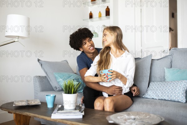 A couple sits together on a comfortable couch, sharing a warm moment with coffee. The bright and inviting living room enhances the cozy vibe, complete with modern decor