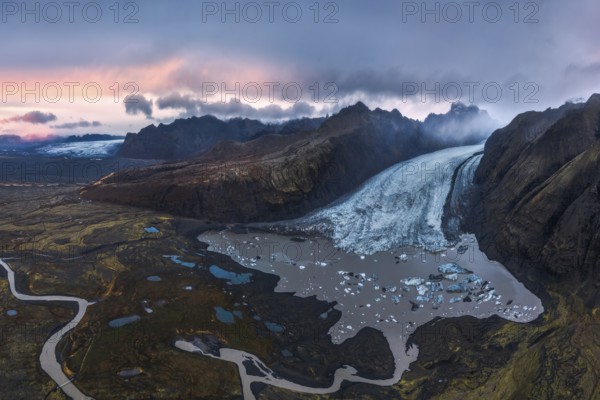 Stunning aerial shot capturing the expansive Vatnajökull Glacier winding through rugged mountains in Vatnajökull National Park, Iceland, under a colorful dusk sky