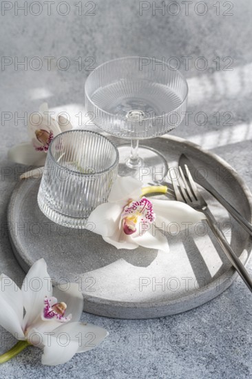 A refined dining setup featuring ribbed glassware, delicate orchids, and sleek cutlery on a circular concrete tray, creating a sophisticated and serene atmosphere