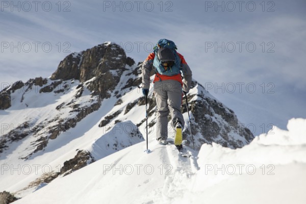 A skier in vibrant gear ascends a snowy peak, showcasing the thrill and challenge of ski touring amidst breathtaking mountain scenery under a clear blue sky
