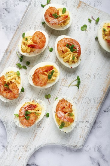 Boiled eggs stuffed with yolk and seasoned with mayonnaise, stuffed eggs with shrimp, on a white wooden chopping board, selective focus, close-up, without people