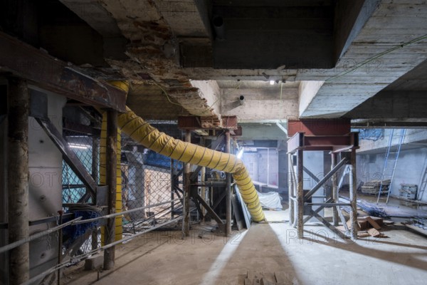 A construction site undergoing structural reinforcement features steel supports, exposed concrete beams, and a large ventilation duct. The dimly lit underground space highlights the ongoing renovation work