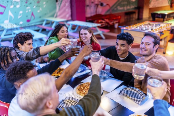 Group of cheerful multi ethnic friends toasting drinks while enjoying a meal together at a bowling alley restaurant