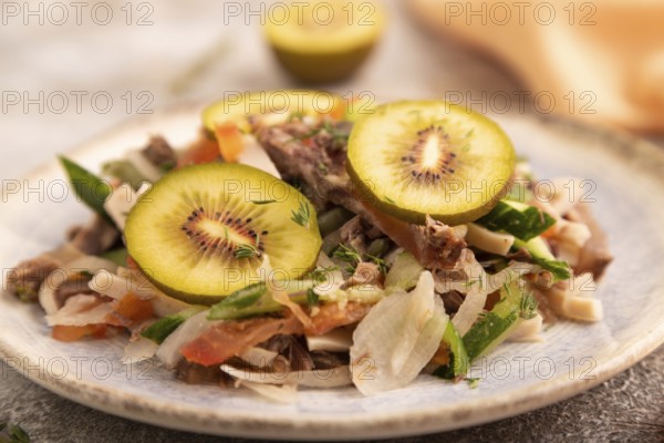 Meat salad with beef kiwi and vegetables on brown concrete background and orange linen textile. side view, close up, selective focus