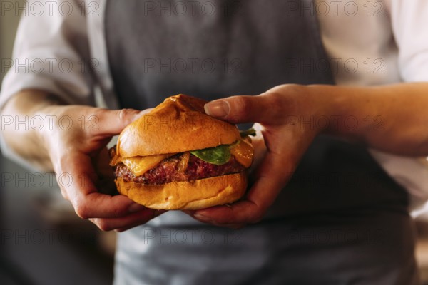 Close-up of an artisan burger presented by a chef. Brioche bun, juicy beef, and melted cheese take center stage in this food image